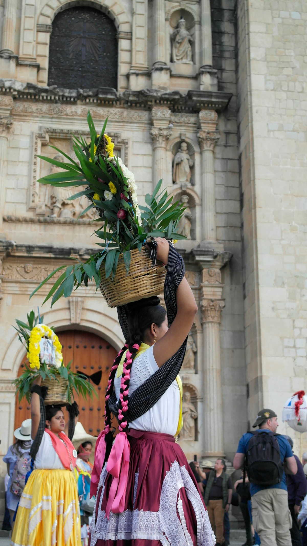 Traditional Oaxacan woman in festival dress carrying a flower basket headdress in front of Santo Domingo cathedral, Oaxaca