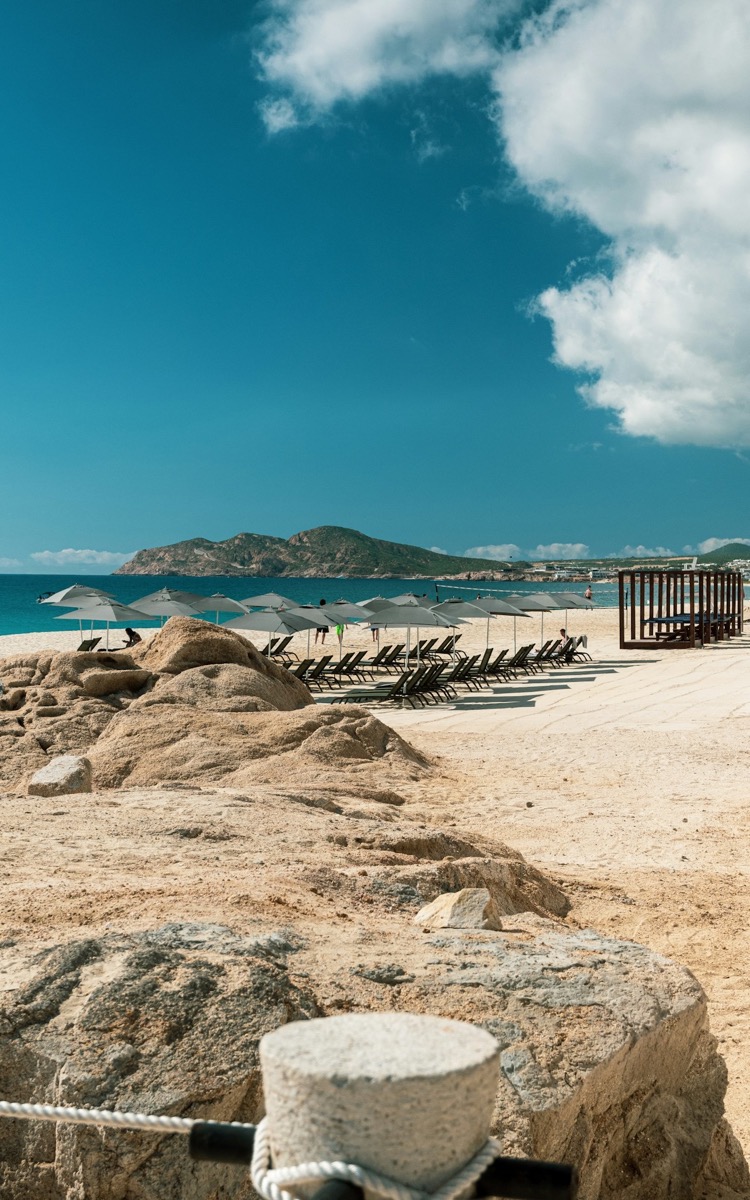 Cabo San Lucas beach with sun loungers, umbrellas, and the Sea of Cortez mountains in the background