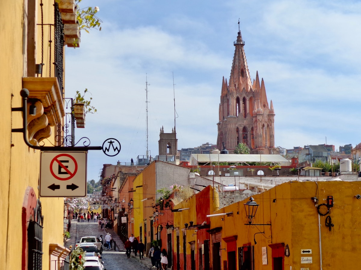 Colourful colonial buildings lining a cobblestone street with a church spire, San Miguel de Allende, Mexico