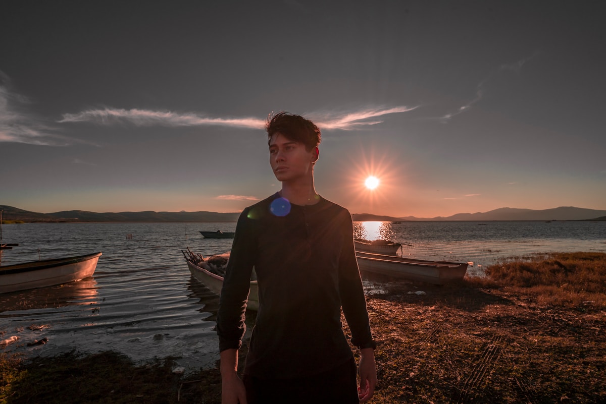 Man standing by lake at sunset with fishing boats, Michoacán, Mexico