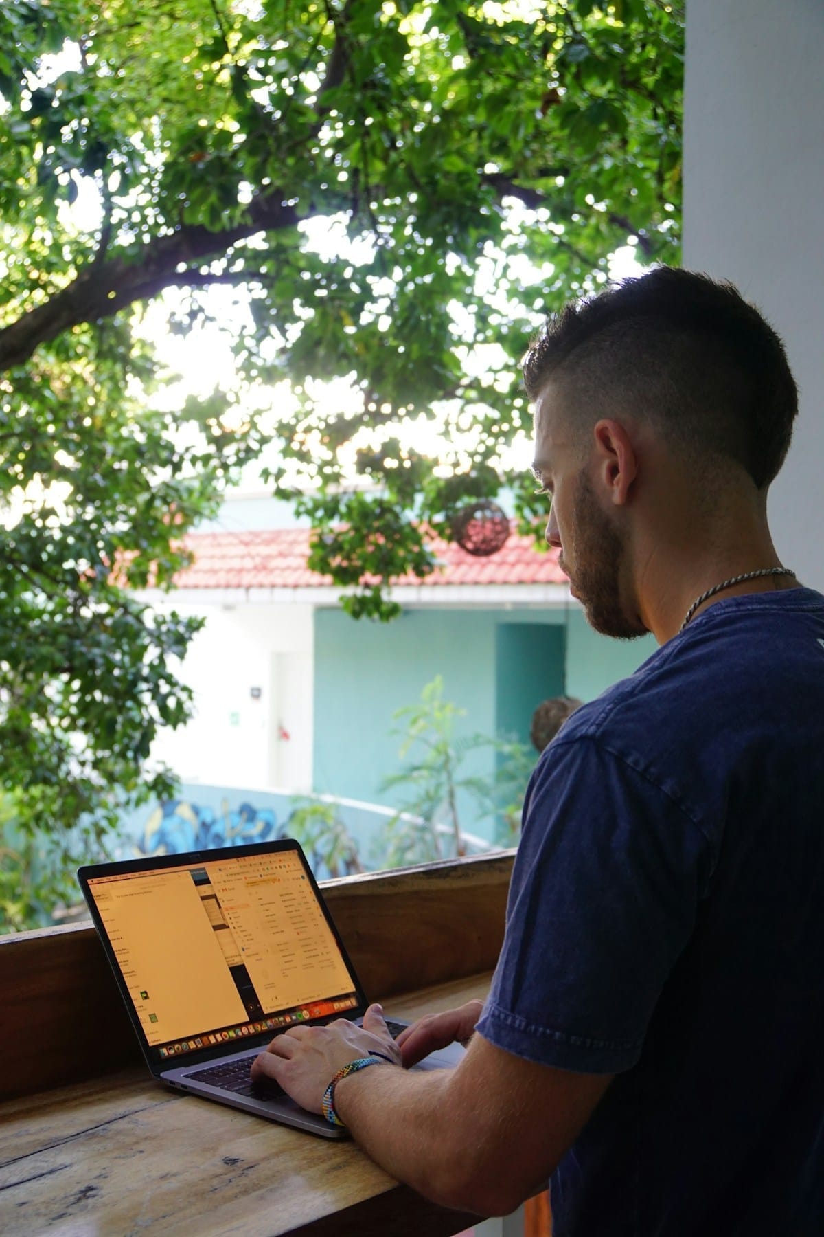 Digital nomad working on laptop at a wooden bench in a tropical Mexican setting, Playa del Carmen