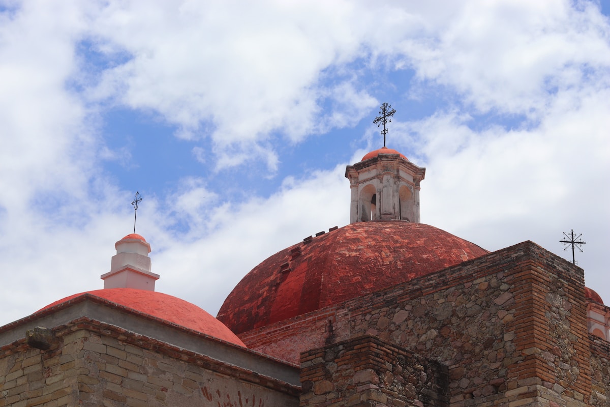 Colonial church with terracotta red dome and stone cross against blue sky, Oaxaca, Mexico