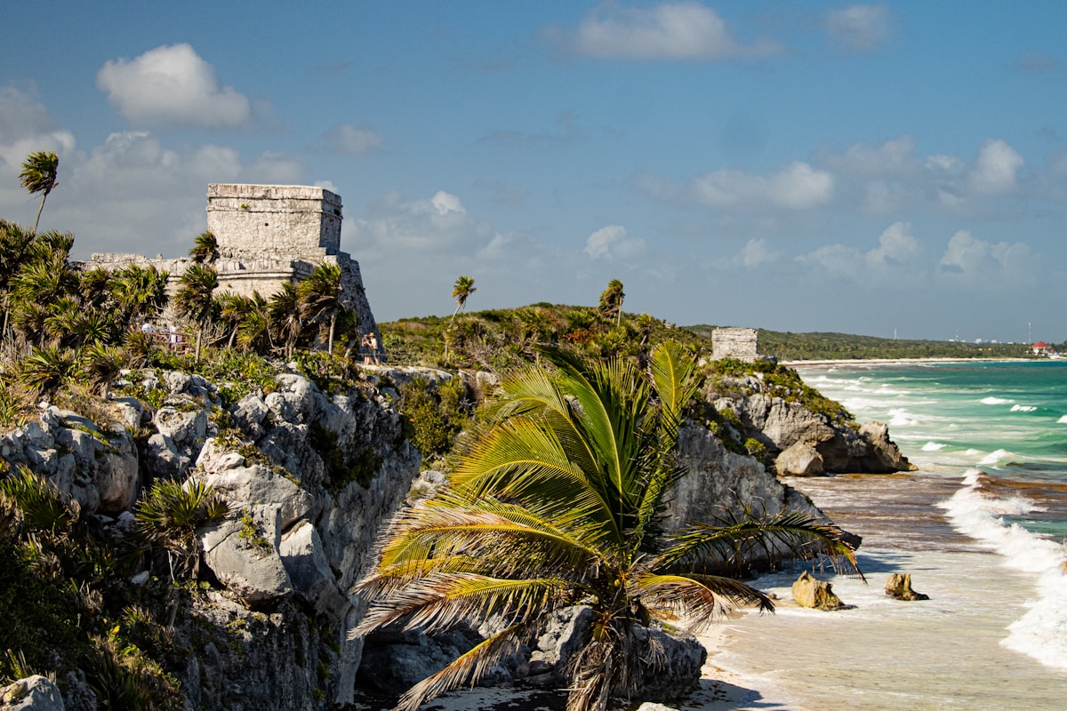 Tulum Maya ruins on rocky cliff overlooking turquoise Caribbean sea with palm tree in foreground