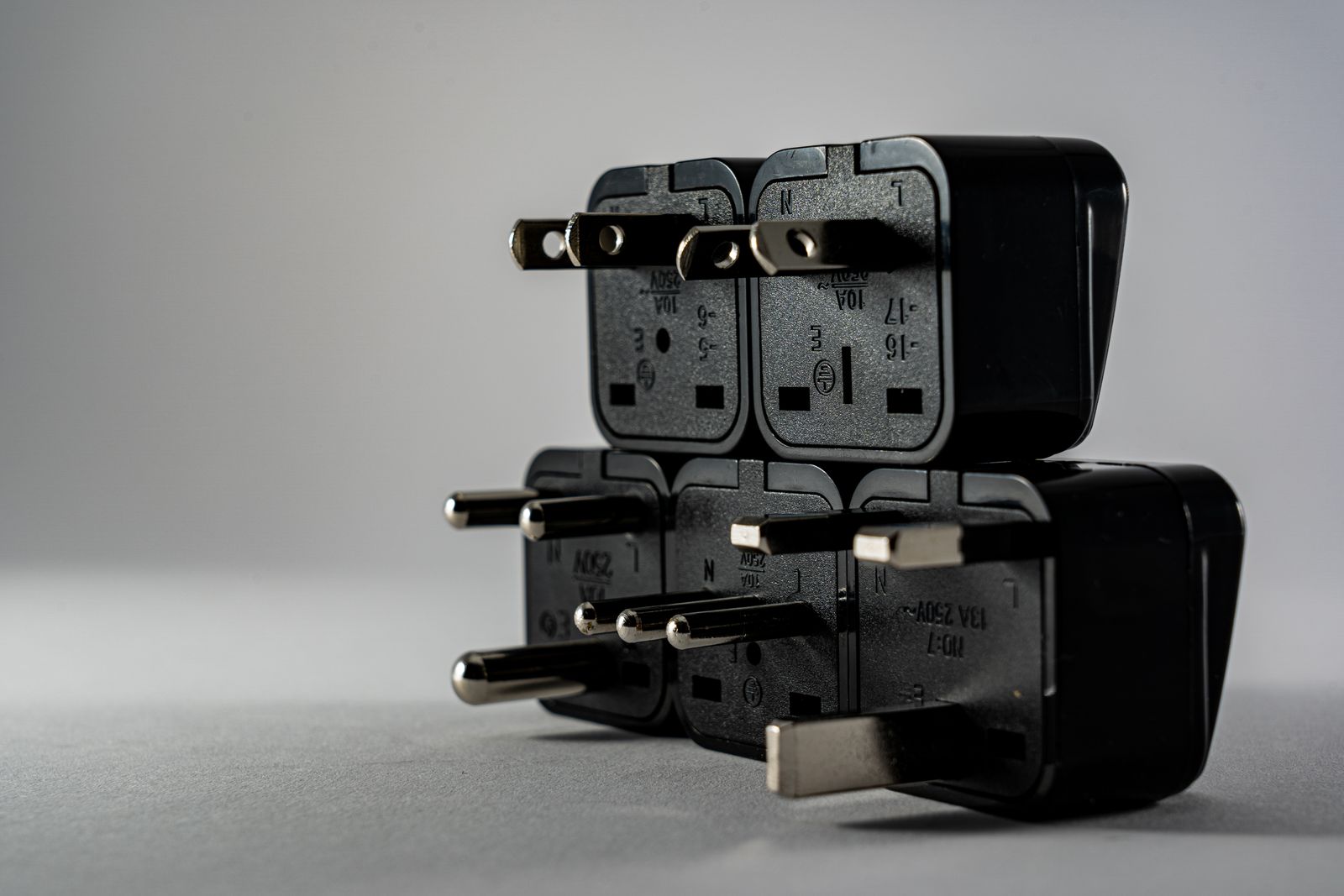 Stack of black travel plug adapters with different pin shapes on a grey background