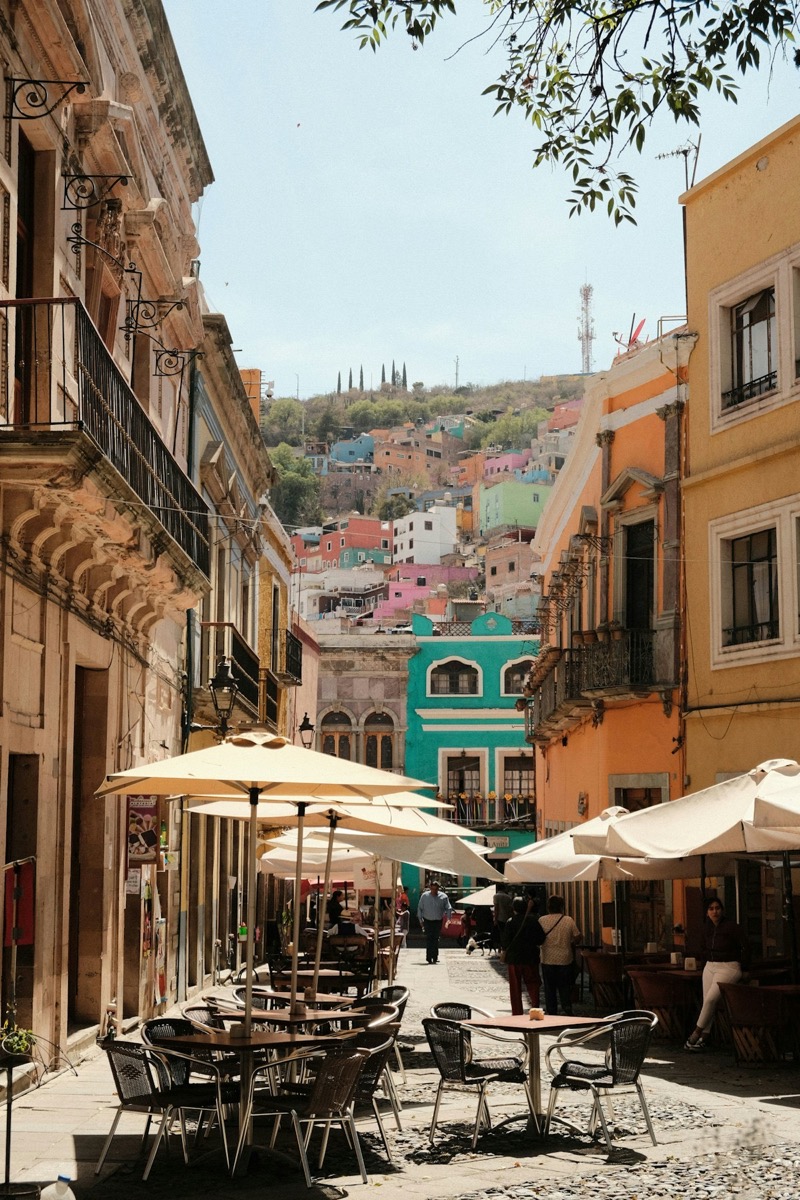 Colourful pedestrian street in Guanajuato with open-air restaurant tables and umbrellas under blue sky