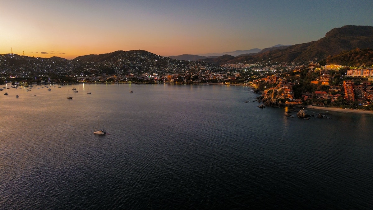 Aerial view of Zihuatanejo bay at sunset with boats on calm water and hillside city lights